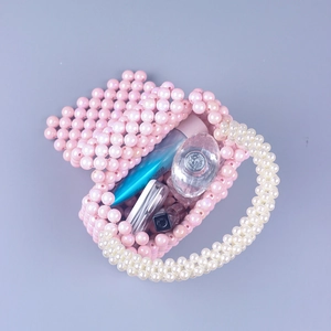Mini pink pearlescent acrylic beaded handbag with top handle for women displayed with makeup