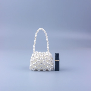 Miniature handmade pearl beaded handbag next to a lipstick showing the compact size