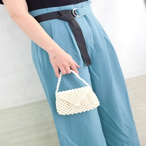 Detail of white faux pearl beaded dumpling bag with handle held by a model