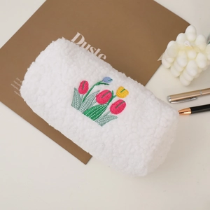 White fuzzy plush makeup bag featuring colorful tulip embroidery on a desk surface