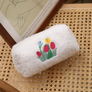 Plush white lamb wool cosmetic bag with colorful tulip embroidery on vintage rattan surface