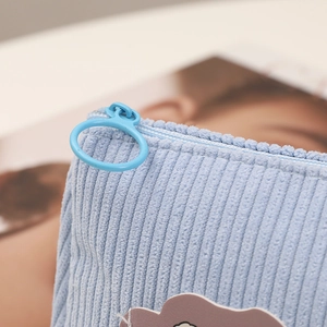 Macro shot of light blue corduroy fabric with round zipper pull and cloud embroidery