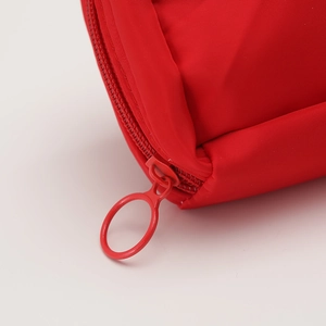 Detailed close-up of a red fabric pencil case featuring a round metal zipper puller