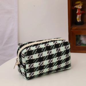 Close-up of green and black tweed checkered makeup bag with zipper detail and soft texture