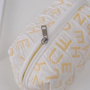 Detail of white quilted fabric with yellow letters and smooth silver zipper puller