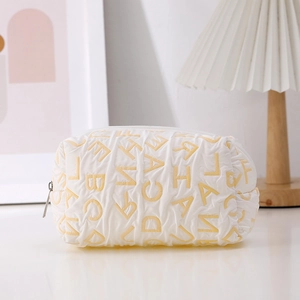 Close-up of white quilted canvas pencil case with yellow letter print and silver zipper