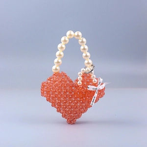 Detail of handmade heart-shaped orange beaded handbag with white pearl handle and ribbon