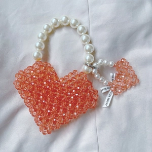 Detail of heart-shaped orange beaded handbag with pearl handle and ribbon charm