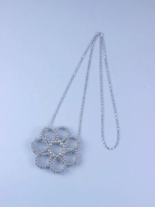 Macro detail of silver hollow flower pendant with beaded texture on a square link chain
