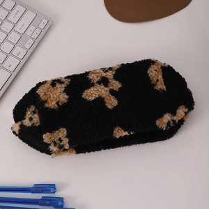 Close-up of black plush cosmetic bag with teddy bear pattern on a desktop with accessories