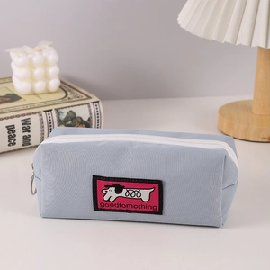 Detailed view of light blue fabric pencil case with dog tag on minimalist white desk