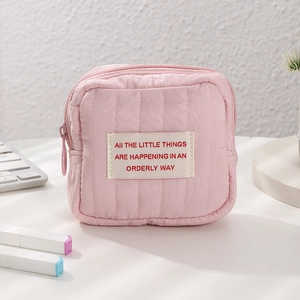 Close-up of pink quilted mini cosmetic pouch with metal zipper on a desk with accessories