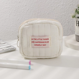 Detail of white quilted mini cosmetic bag with zipper pull on a minimalist desk