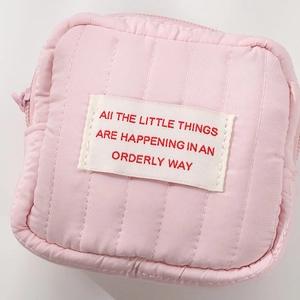 Pink quilted mini cosmetic bag with a white woven text label and smooth zipper