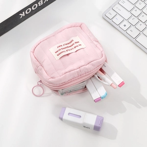 Close-up of pink quilted mini cosmetic bag with ring zipper on a clean white desk setup