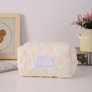 Detail of cream quilted makeup bag with yellow heart embroidery and zip closure