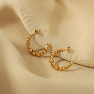 Classic gold-plated stainless steel C-shaped beaded hoop earrings on beige textured fabric