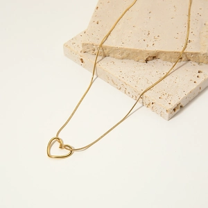 Détail d'un collier pendentif cœur évidé doré avec une chaîne serpent sur pierre