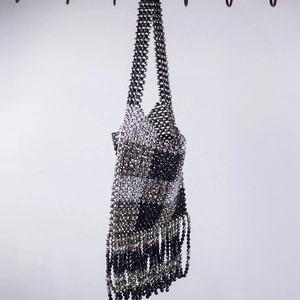 Detail of handmade beaded handbag featuring black and silver geometric weave and long tassels