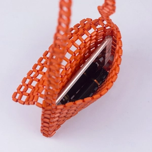 Detail showing the orange beaded bag interior holding a smartphone and lipsticks