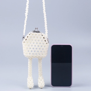 Détail du sac bandoulière perlé fait main montrant sa mini taille à côté d'un smartphone