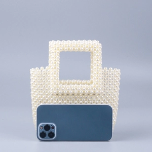 Detailed close-up of handmade faux pearl woven handbag with square cutout handles