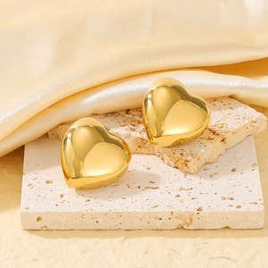 Polished 18k gold heart stud earrings displayed on travertine stones and silk fabric