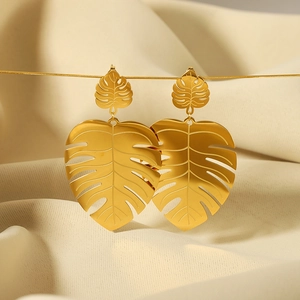 Elegant 18k gold plated stainless steel monstera leaf drop earrings on cream fabric
