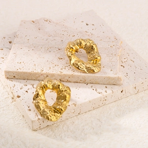 Close-up of golden hammered stainless steel earrings on a minimalist stone background