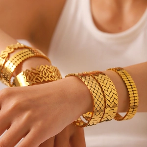 Dettaglio di bracciali a strati in acciaio al titanio dorato con motivi a foglia e maglia