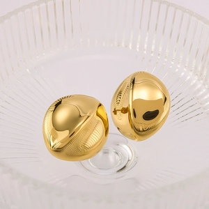 Macro shot of polished gold-plated bean stud earrings displayed in a textured glass dish