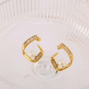 Vue détaillée de boucles d'oreilles dorées avec perle centrale et zircons incrustés