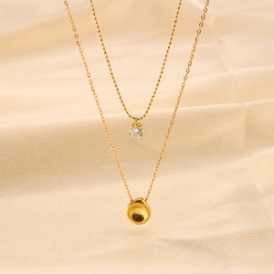 Gold double-layered necklace with zircon pendant and irregular metal charm on silk background