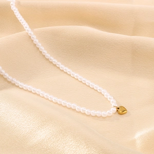 Detailaufnahme des Herzanhängers an einer weißen Perlenkette auf Satin-Stoff