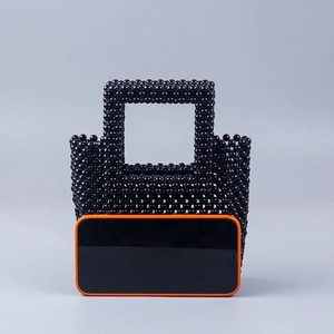 Sac à main artisanal en perles noires avec anses à côté d'un téléphone pour la taille