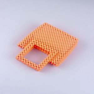 Macro detail of high-gloss orange acrylic beads on handmade woven square handbag