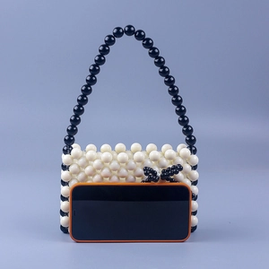 Detailed view of handmade beaded tote with black bow accent next to a smartphone