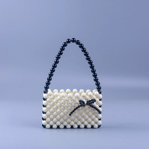 Close-up of handmade cream acrylic beads with a black beaded bow on the handbag