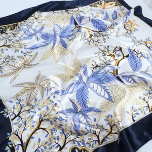 Détail d'un foulard en soie avec feuilles bleues et jaunes, texture satinée et bordures