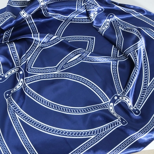 Macro view of dark blue satin silk scarf showing geometric chain and horseshoe patterns