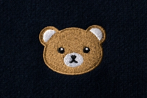 Detailed close-up of brown bear embroidery on dark blue knitted fabric for children