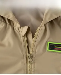 Detail of khaki windbreaker showing zipper and HIGHER badge on waterproof fabric