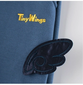 Detalle del bordado Tiny Wings y parche de ala de satén azul en pantalones de niños