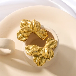 Polished 18K gold-plated stainless steel leaf earrings shown on a white ceramic display