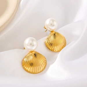 Gros plan de boucles d'oreilles coquillage dorées avec perles sur tissu de soie blanc