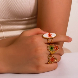 Dettaglio del set di anelli dorati vintage con inserti in resina e fiori secchi rossi