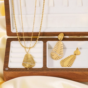 Gold stainless steel leaf jewelry set with necklace and earrings on a wooden box