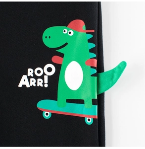 Detail van zwarte kinderbroek met een cartoon dinosaurus op skateboard en 3D-staart