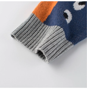 Detail of grey ribbed cuff and dinosaur pattern on knit sweater with orange accents