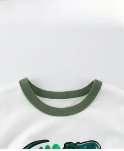 Détail du col rond avec bordure côtelée verte et motif de dinosaure sur un T-shirt en coton blanc